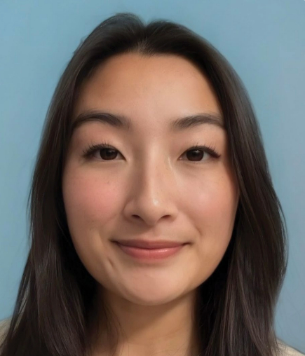 A young woman with long, dark hair smiles softly in front of a plain light blue background. She has clear skin, natural makeup, and is facing the camera.